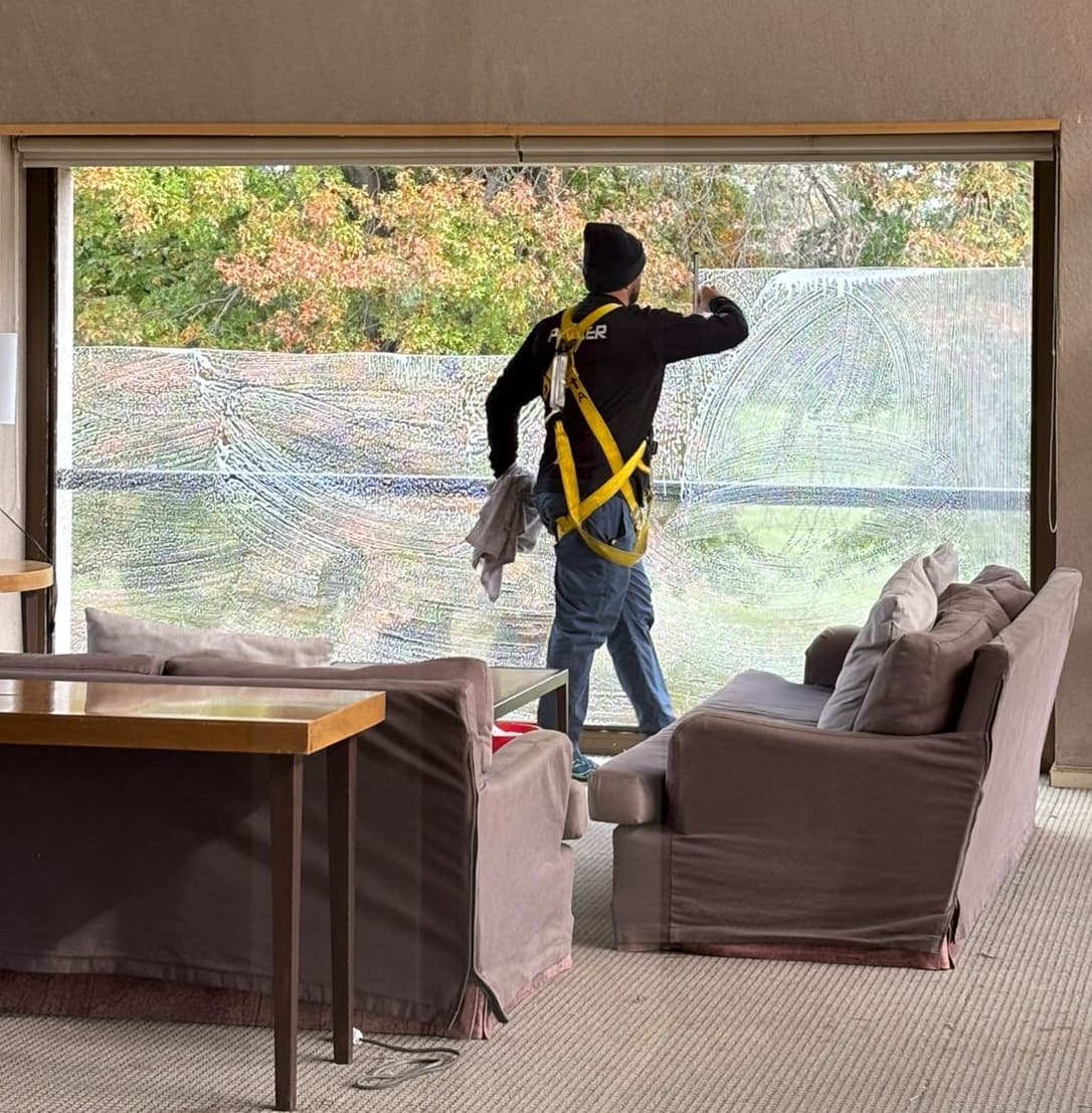Window cleaning technician in safety harness cleaning a large picture window with Denver fall foliage outside